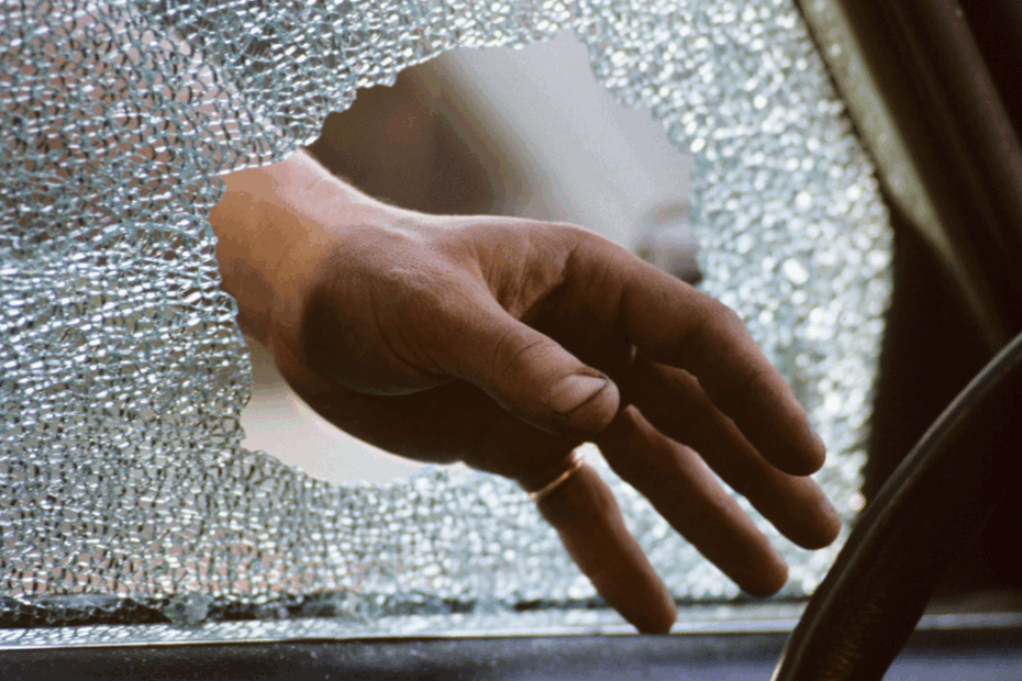 Pessoa quebrando o vidro de um carro durante um roubo.