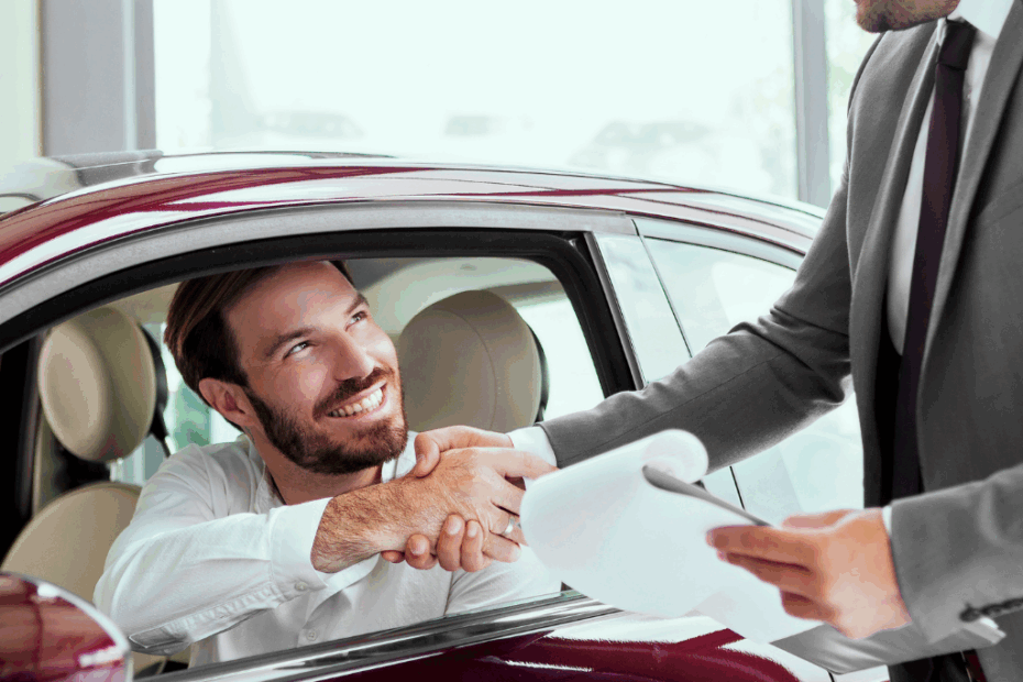 Homem dentro de um carro apertando a mão de outro homem, representando o fechamento da compra de um carro, por meio do consórcio